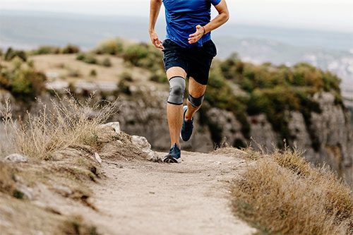 Person with runner’s knee jogging on nature trail while wearing knee braces