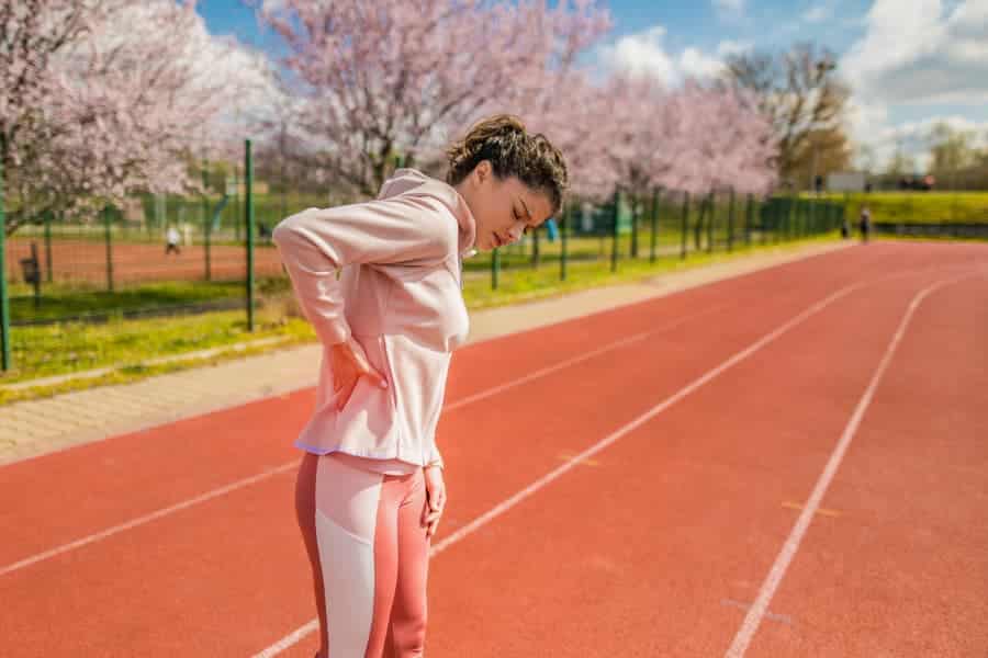 Young athlete standing on a track placing hand on area of back pain