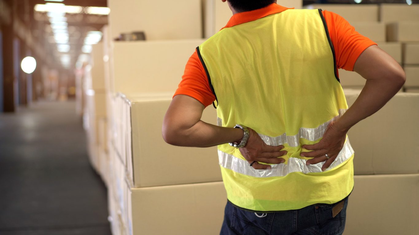 Worker in warehouse with boxes placing hands on lower back