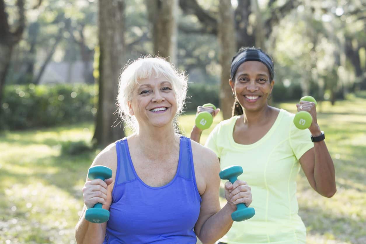 Two people walking outside wearing exercise clothing and holding hand weights