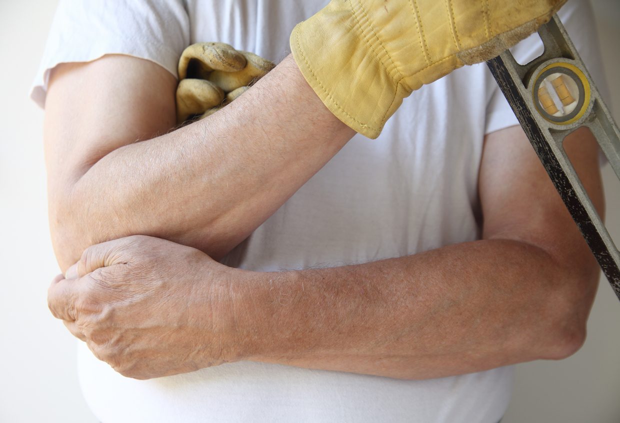 Construction worker holding elbow in pain due to elbow arthritis