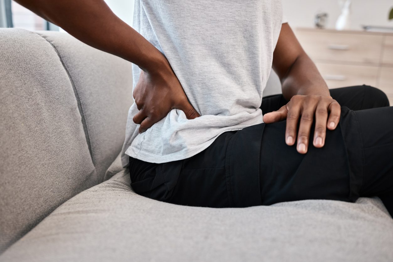 Younger patient sitting on couch grabbing hip in pain