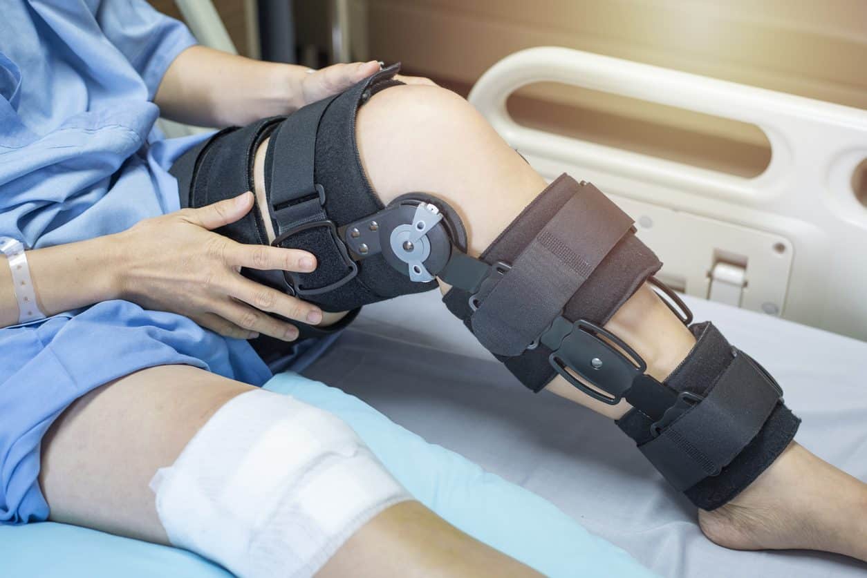 Patient in hospital bed with knee bandage on one leg and knee brace on other leg