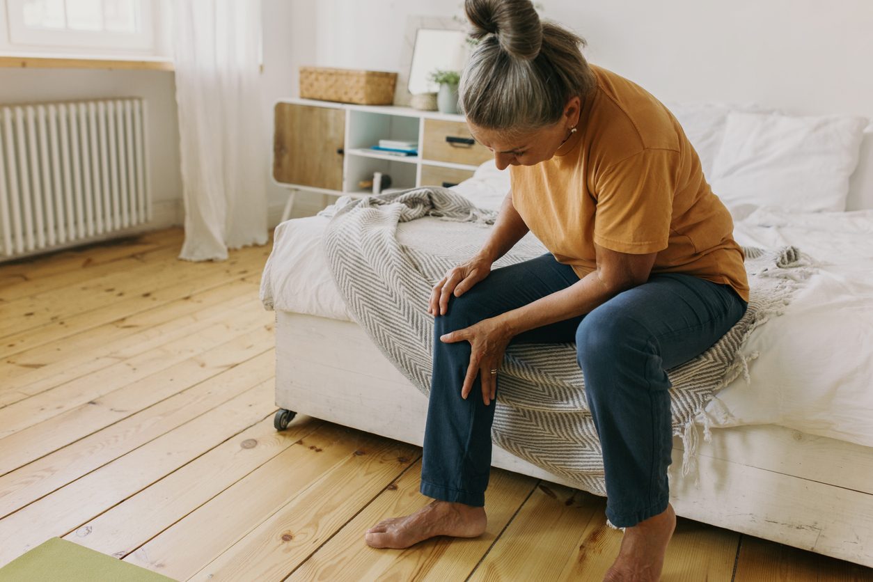 Person grabbing knee in pain while sitting on bed in bedroom
