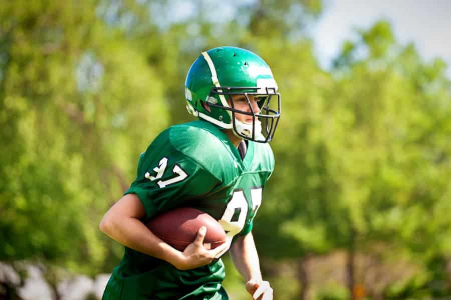 High school football player in green uniform with football tucked in arm