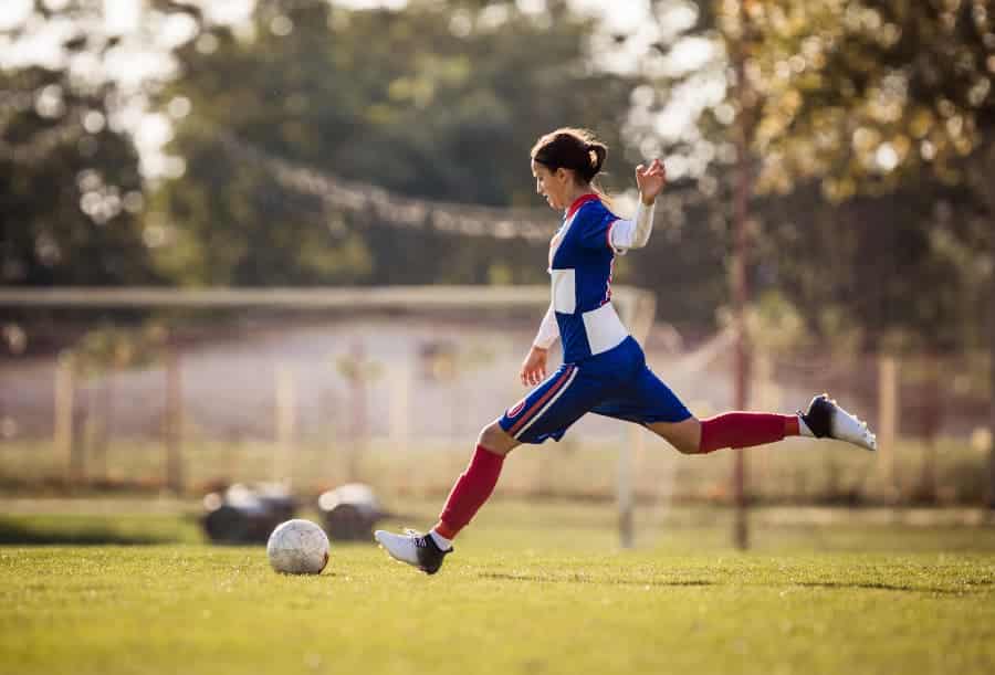 High school soccer player kicking ball down field in red, white and blue uniform