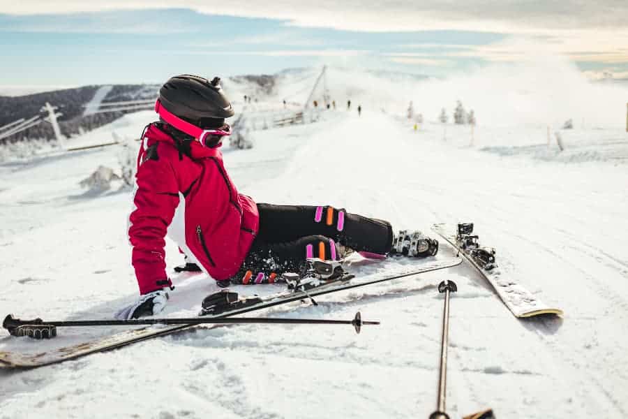 Injured skier sitting on snow-covered mountain, surrounded by gear