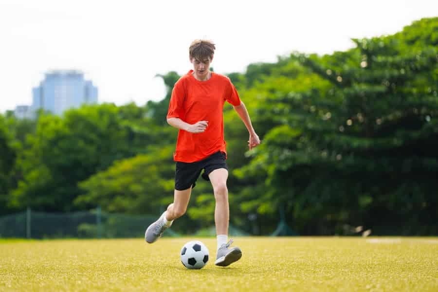 Teenage soccer player practicing on field in red shirt and black shorts