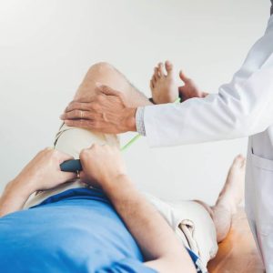 Sports medicine physician examines mobility of patient’s knee using resistance band