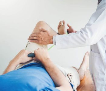 Sports medicine physician examines mobility of patient’s knee using resistance band